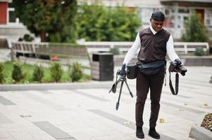 jovem cinegrafista americano africano profissional segurando câmera profissional com equipamento profissional. cinegrafista afro vestindo duraq preto fazendo vídeos. foto