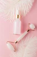 conjunto cosmético de spa em casa. rolo de quartzo rosa para massagear rosto e corpo e óleo de beleza natural com penas brancas macias