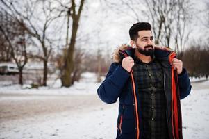 homem indiano de barba usa jaqueta em dia frio de inverno. fones de ouvido móveis nos ouvidos. foto