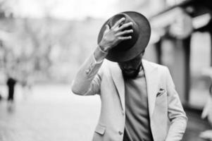 homem afro-americano elegante usa jaqueta bege e pose de chapéu preto na rua. foto