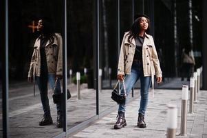 elegante mulher afro-americana usar boina e casaco com bolsa posando ao ar livre. foto