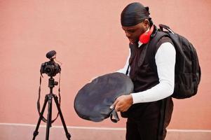 jovem cinegrafista americano africano profissional segurando câmera profissional com equipamento profissional. cinegrafista afro vestindo duraq preto fazendo vídeos. foto