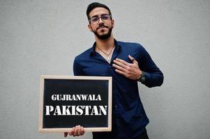 homem árabe usa camisa azul e óculos segura placa com inscrição gujranwala paquistão. maiores cidades no conceito do mundo islâmico. foto