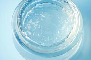 um recipiente de vidro com gel hidratante em um fundo azul. gel transparente com bolhas. foto