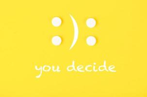 quatro comprimidos brancos na forma de um emoticon triste e alegre. o texto que você decidir. fundo amarelo. foto
