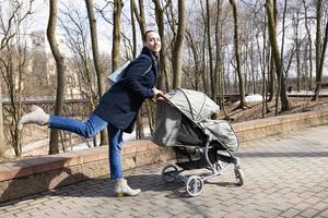 dia das Mães. jovem andando no parque primavera com carrinho de bebê. mãe passa tempo com seu filho ao ar livre foto