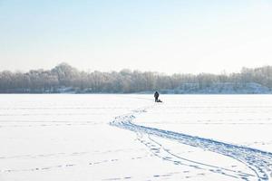 um velho eremita solitário, no inverno, atravessa o rio no gelo e puxa um trenó com lenha para aquecimento foto