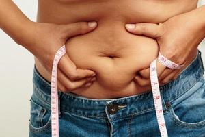 homem gordo confira corpo com excesso de peso abdômen sua barriga com fita métrica na mão foto