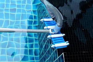 trabalhador limpa piscina privada com aspirador de tubo azul a vácuo todas as semanas no verão foto