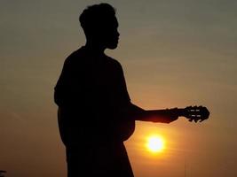 silhueta de uma pessoa tocando guitarra em um fundo por do sol foto