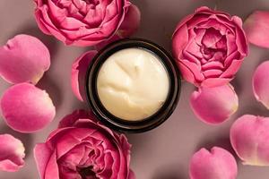 frasco aberto de creme de ervas natural para mulheres em fundo rosa pastel. lindas rosas cor de rosa. flores frescas. conceito de rotina diária de cuidados com a pele. foto