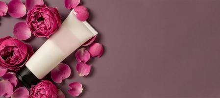 tubo cosmético em branco com creme em um fundo rosa escuro com flores rosas. creme, gel, tubo, embalagem do produto, lugar para texto. pronto para o seu design de embalagem. bandeira foto