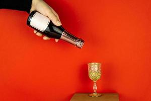 mão feminina segurando uma pequena garrafa de champanhe no fundo vermelho. maquete com espaço de cópia. foto