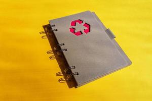 planejador de notebook com sinal de reciclagem em uma capa em fundo laranja. conceito de reciclagem de resíduos. foto