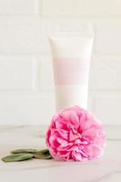 tubo rosa com creme de rosto ou corpo rosa ou esfoliante decorado com flores de núcleo rosa. conceito de cuidados com a pele. maquete de desmarcação foto