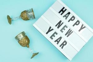 caixa de luz de feliz ano novo com taças de champanhe dourado sobre fundo azul. foto