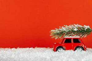 pequeno carro de brinquedo vermelho carregando spruse em uma estrada de neve. cartão festivo de natal. foto