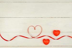 composição romântica criativa de dia dos namorados com corações vermelhos, fita de cetim em fundo de madeira. maquete com espaço de cópia para blogs e mídias sociais. foto