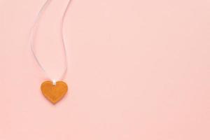 pingente de forma de coração dourado em uma fita branca sobre fundo rosa. conceito festivo de dia dos namorados com espaço de cópia. vista do topo foto
