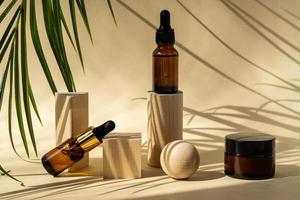 frascos de cosméticos âmbar com pipeta em pódios de pedestal geométrico de madeira, embalagem de produtos com folhas de palmeira naturais, soro antienvelhecimento com peptídeos, maquete de cosméticos, conceito de spa. foto