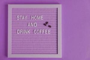 citar ficar em casa e beber café na placa decorativa roxa. decoratina com grãos de café. placa de tipografia para decoração de interiores. foto