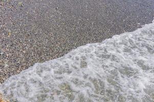 litoral de seixos. beira-mar com água transparente e pequenas pedras foto