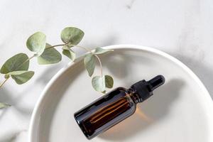 garrafa de vidro âmbar com folhas de eucalipto na bandeja redonda de cerâmica. óleo essencial de rosto e corpo para cuidados com a pele foto