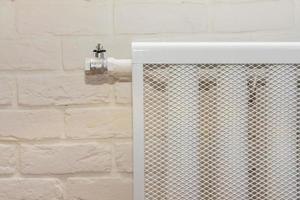 dispositivo de aquecimento do radiador contra uma parede de tijolos brancos. casa aconchegante com quarto interior moderno close-up. foto