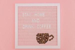 citar ficar em casa e beber café na placa decorativa rosa. xícara feita de grãos de café. slogan de prevenção formulário covid-19. foto