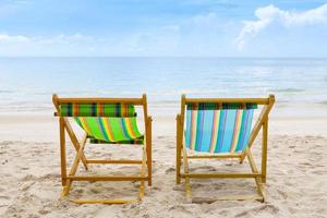 cadeiras de praia na praia de areia branca com céu azul nublado foto
