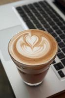 uma xícara de café com leite no teclado do laptop foto