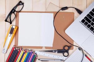 local de trabalho com lápis de cor e suprimentos, laptop, notebook, óculos na mesa de madeira foto
