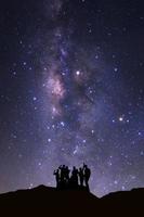 paisagem com via láctea, céu noturno com estrelas e silhueta de pessoas felizes em alta montanha foto