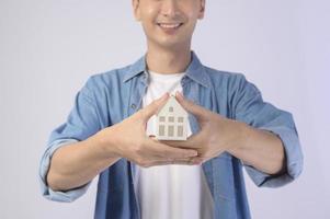 jovem sorridente segurando a pequena casa modelo sobre estúdio de fundo branco foto