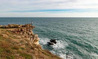 um homem desfruta de uma bela vista para o mar do topo de um penhasco. foto