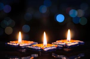 foco seletivo na chama das primeiras lâmpadas de argila diya acesas em fundo escuro com luzes coloridas de bokeh. conceito de festival de diwali. foto