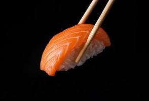 sushi nigiri japonês tradicional com salmão colocado entre pauzinhos, separados em fundo preto foto