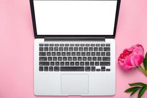 linda flor de peônia rosa e laptop com espaço de cópia para o seu texto em fundo rosa pastel foto