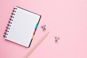 caderno em uma gaiola com lápis em um fundo rosa foto