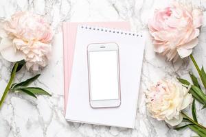 celular com um notebook branco e rosa e flores piony em um fundo de mármore foto