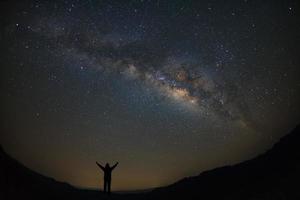 paisagem via láctea com estrelas e silhueta de um homem feliz em pé, fotografia de longa exposição, com grãos. foto