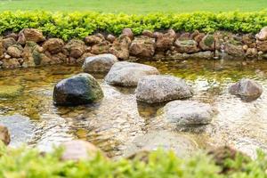 pedra no pequeno rio fumegante criado por humanos no jardim no dia de sol. foto