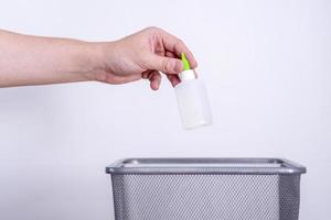 uma mão joga um tubo de plástico no lixo contra um fundo cinza. foto