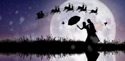 silhueta do Papai Noel à noite de Natal com casal dançando sob a lua cheia. foto