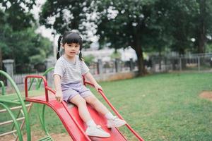 linda garota asiática joga na escola ou jardim de infância ou playground. atividade de verão saudável para crianças. menina asiática escalando ao ar livre no playground. criança brincando no playground ao ar livre. foto