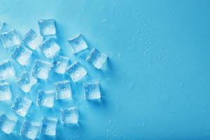 cubos de gelo com gotas de água espalhadas sobre um fundo azul, vista superior foto