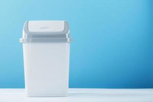 uma lata de lixo branca com tampa em um fundo azul. foto
