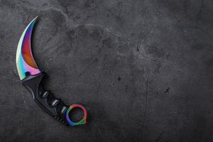 punhal kerambit com uma lâmina cor de arco-íris em um plano de fundo texturizado escuro. foto