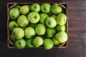 maçãs verdes em uma caixa em uma mesa de madeira, vista superior. foto