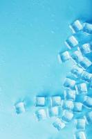 cubos de gelo com gotas de água espalhadas sobre um fundo azul, vista superior foto